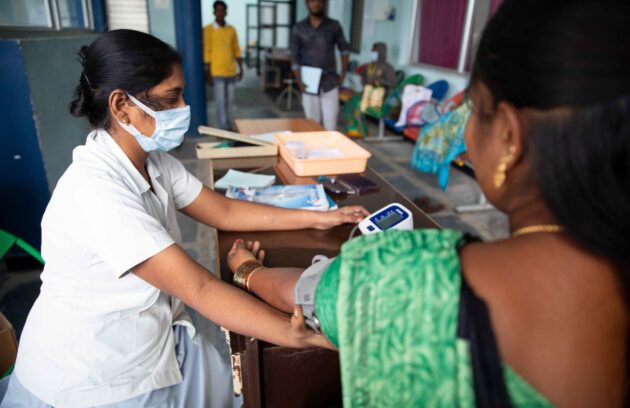 A woman wearing a face mask is checking her blood pressure in the Department of Internal & Family Medicine at Bathalapalli.